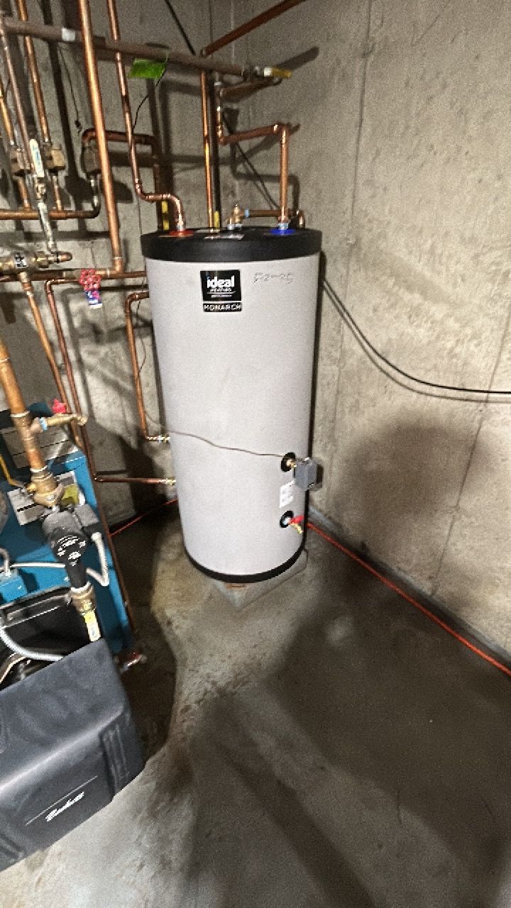A water heater is sitting in a basement next to a boiler.