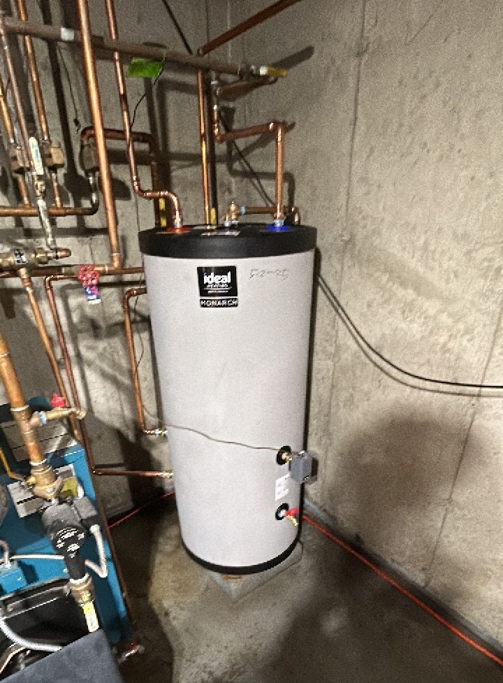 A water heater is sitting in a basement next to copper pipes.