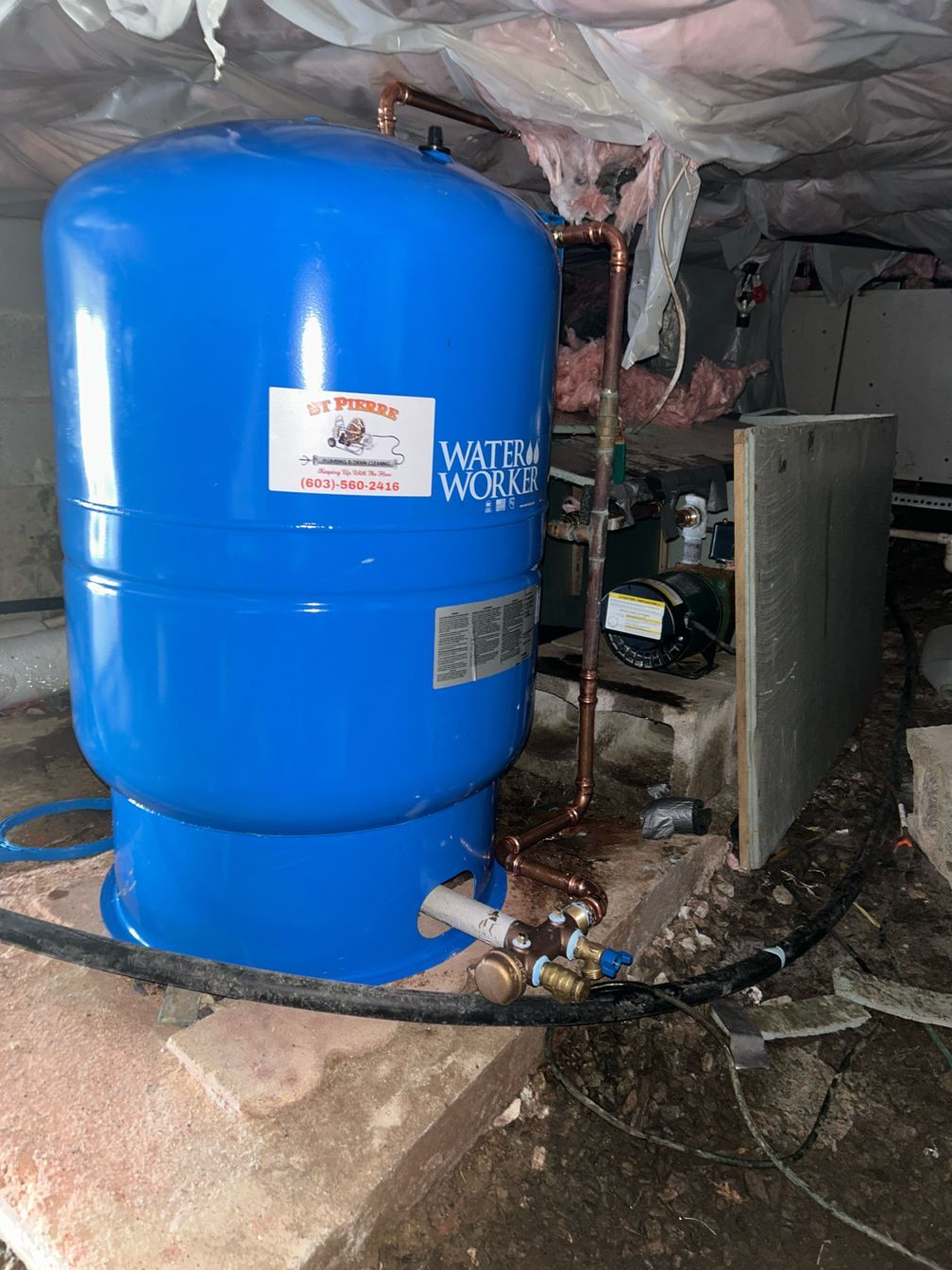 A blue water tank is sitting on the ground in a basement.