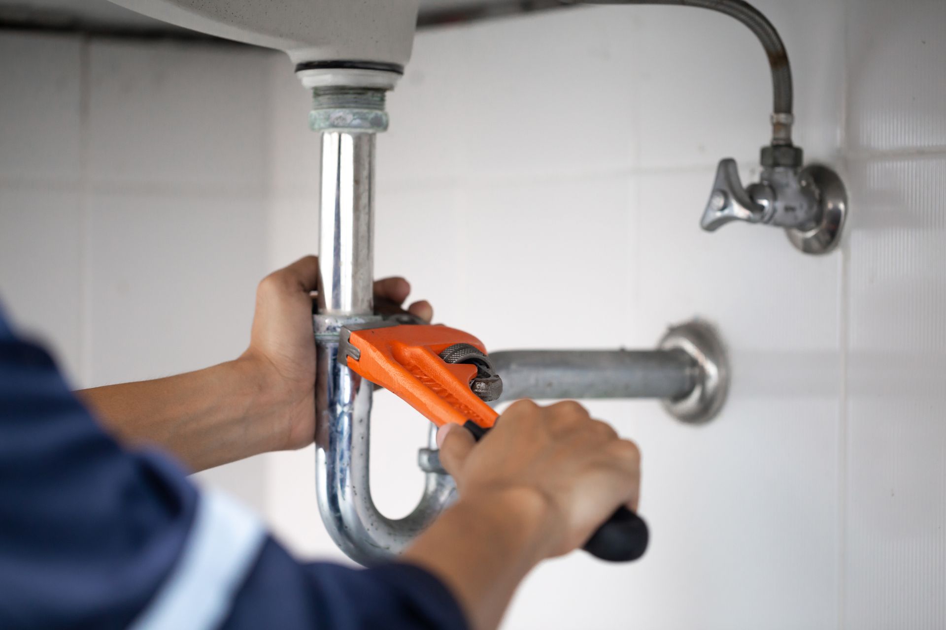 A plumber works in a bathroom, fixing the metal pipes of a water sink.
