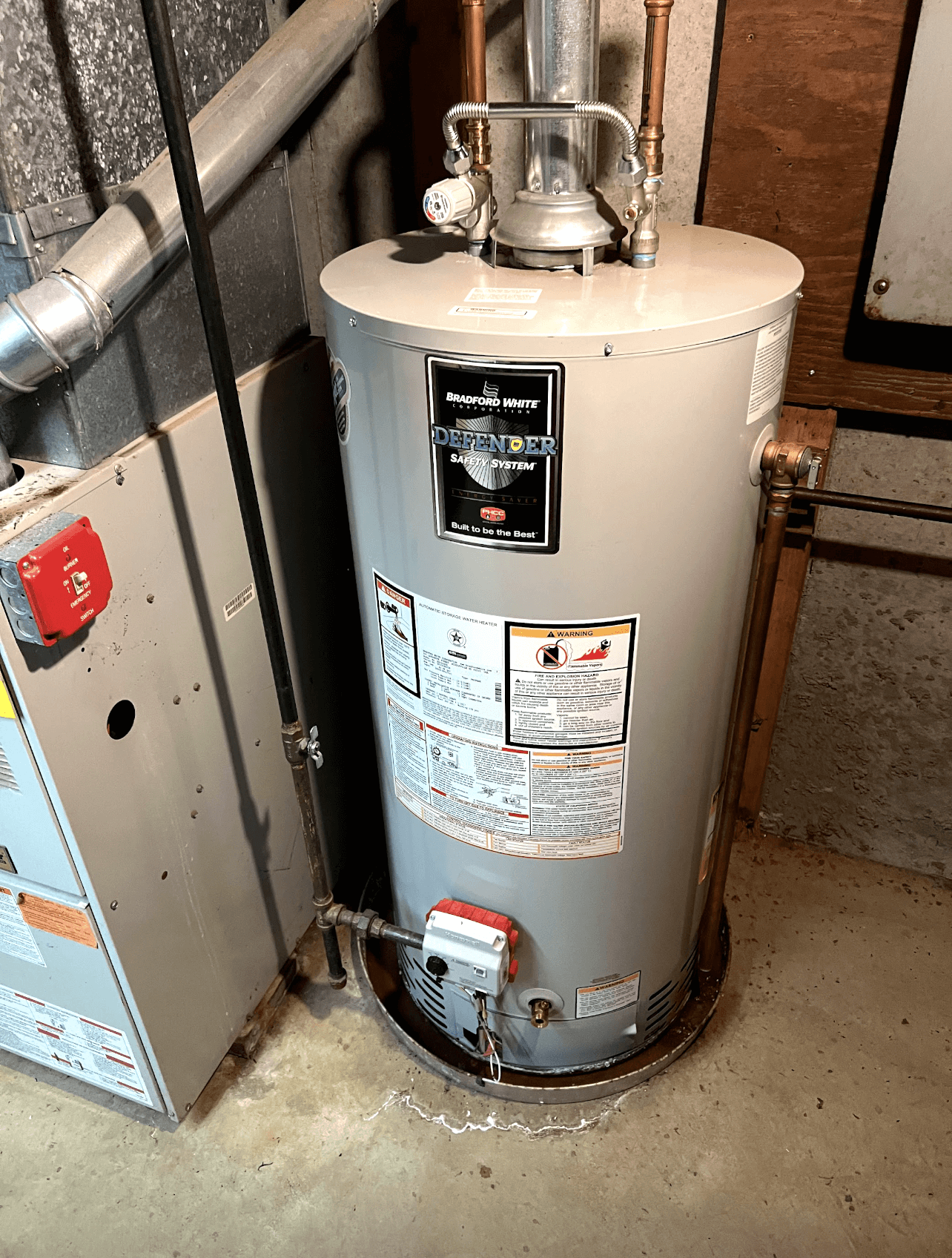 A water heater is sitting next to a furnace in a basement.