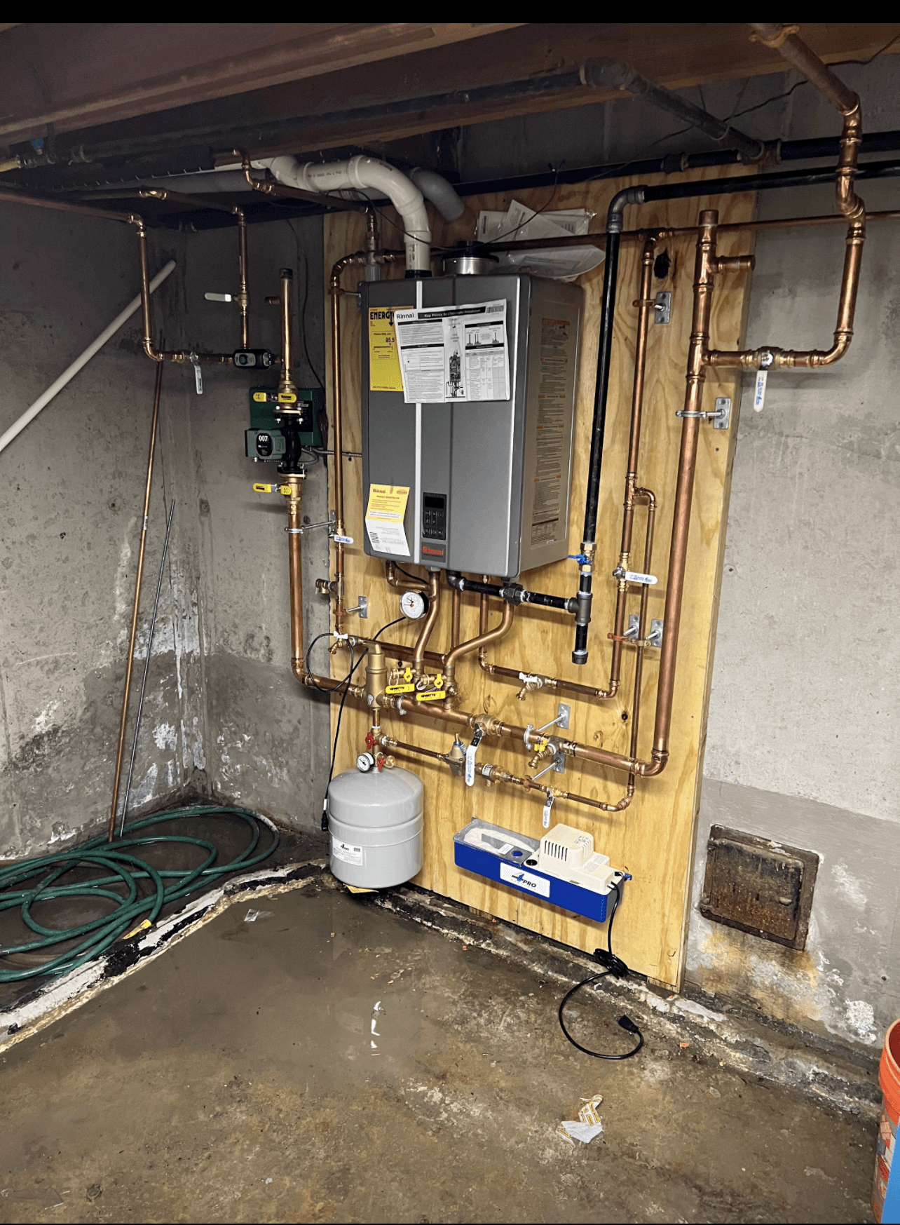 A water heater is sitting on a wooden wall in a basement.