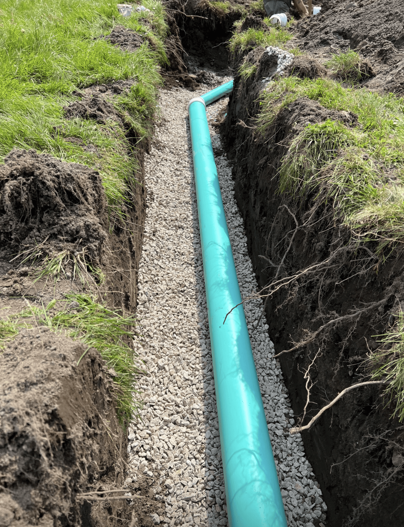 A green pipe is being installed in a trench.