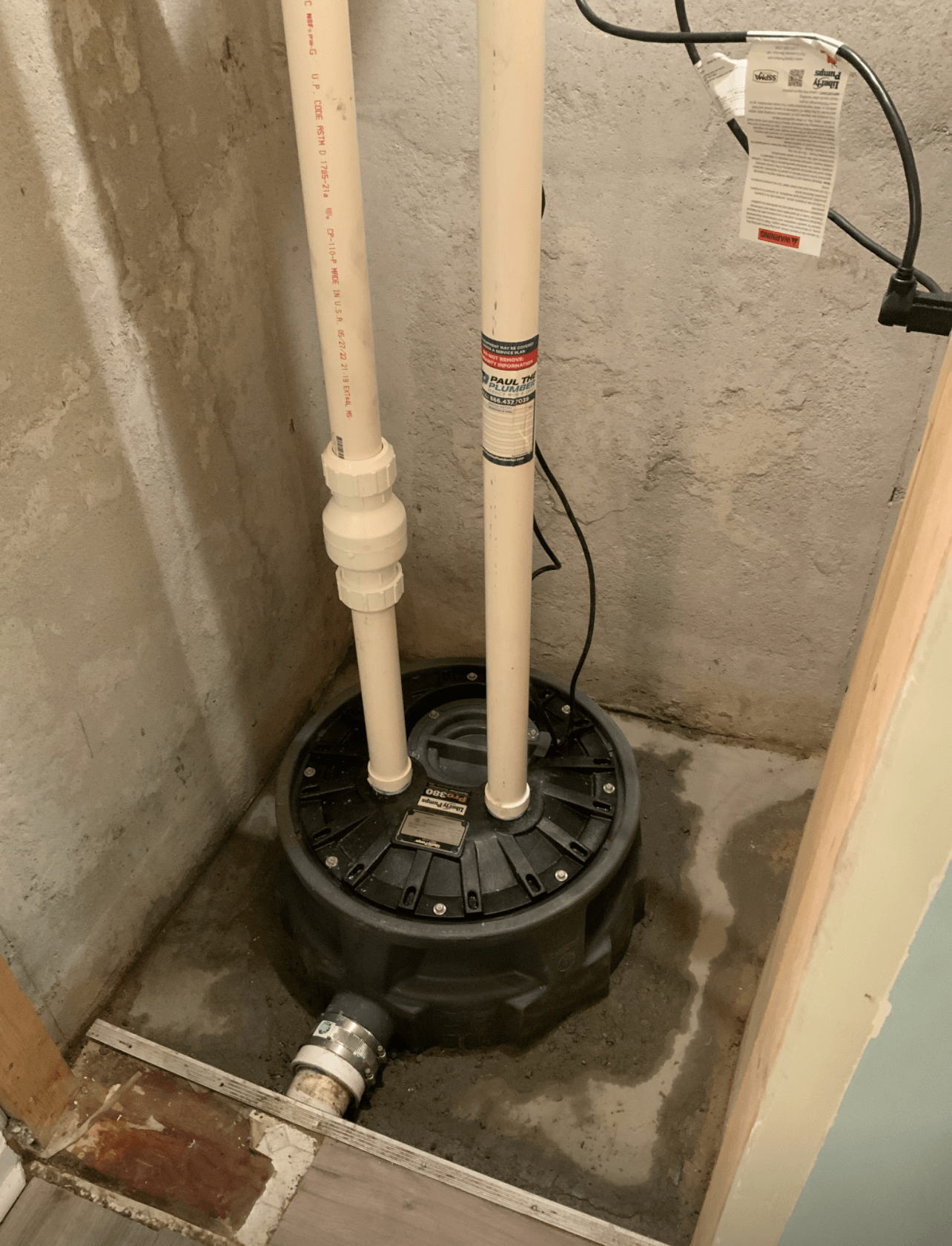 A sump pump is sitting in a basement next to a wall.