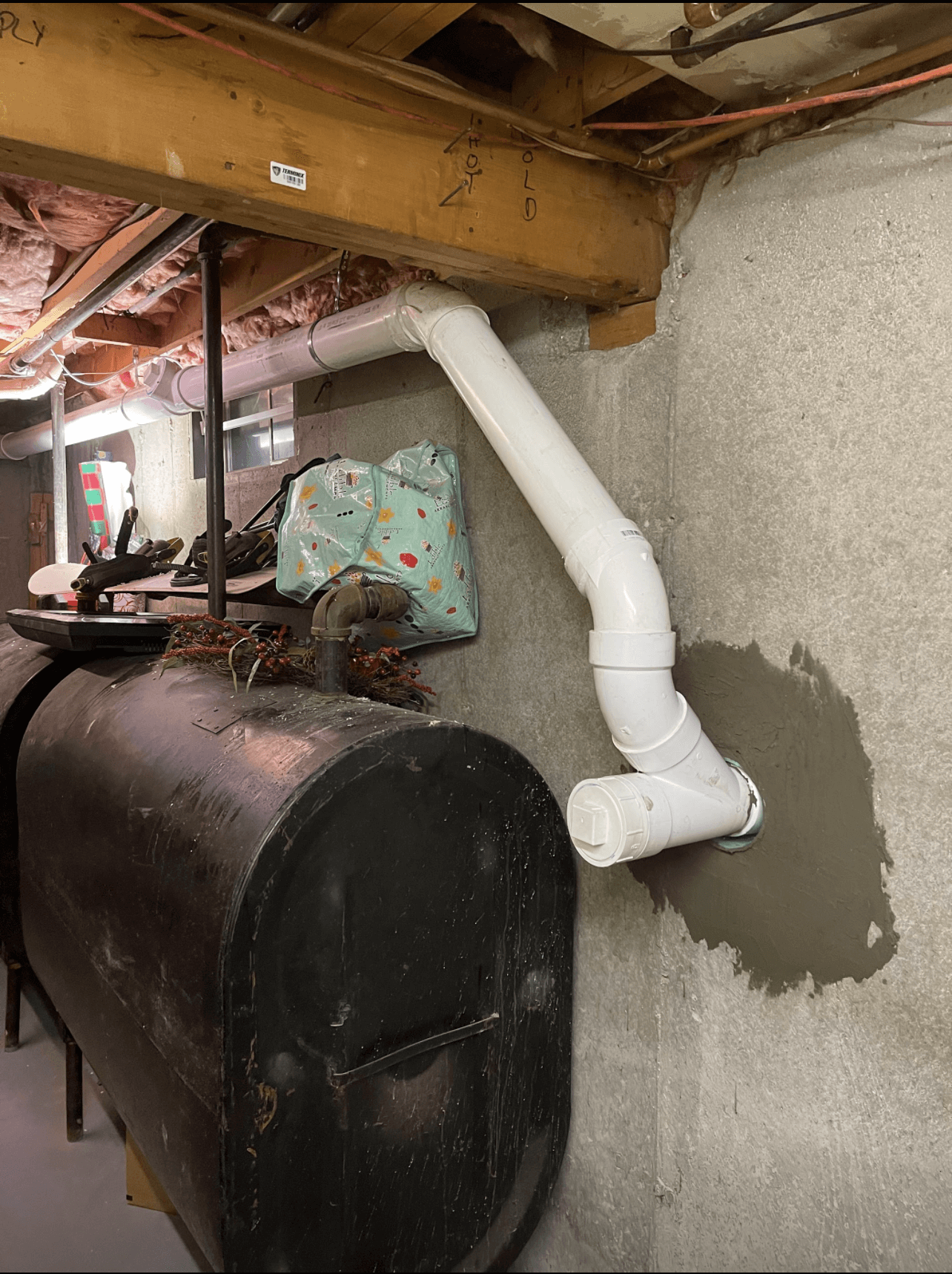 A black tank with a white pipe attached to it in a basement.