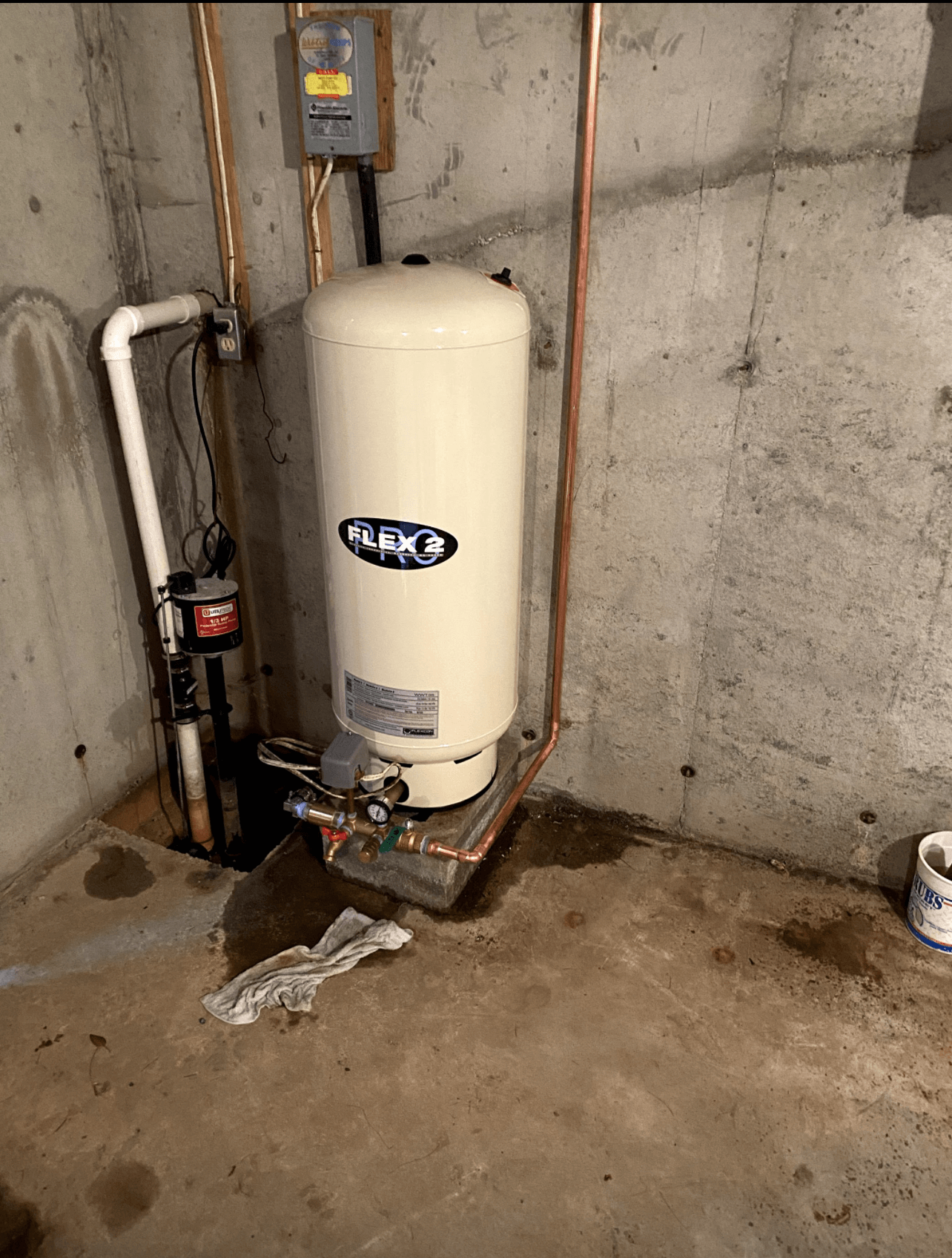 A water heater is sitting in a basement next to a concrete wall.