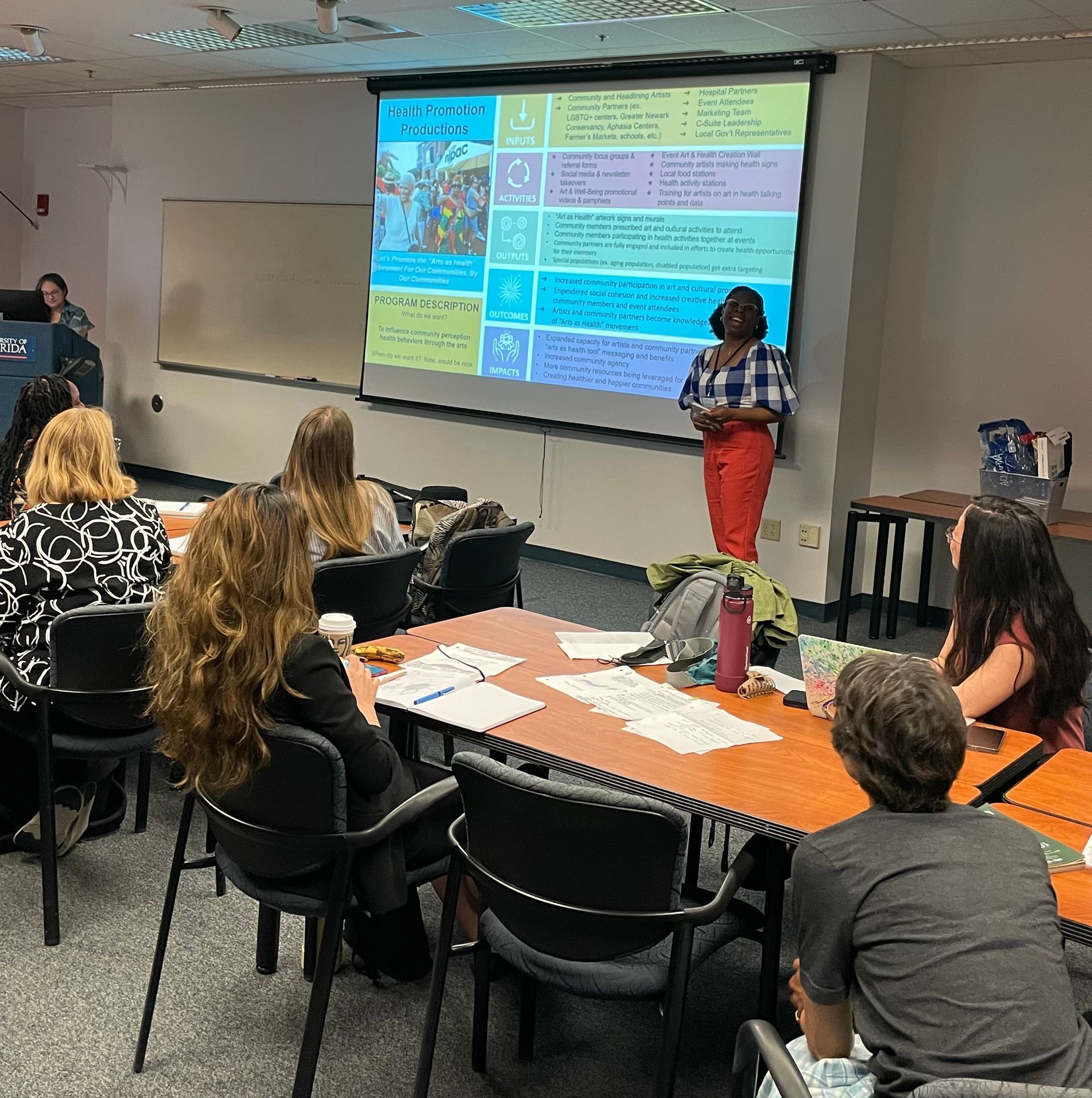A student giving a presentation at the front of a classroom of students.
