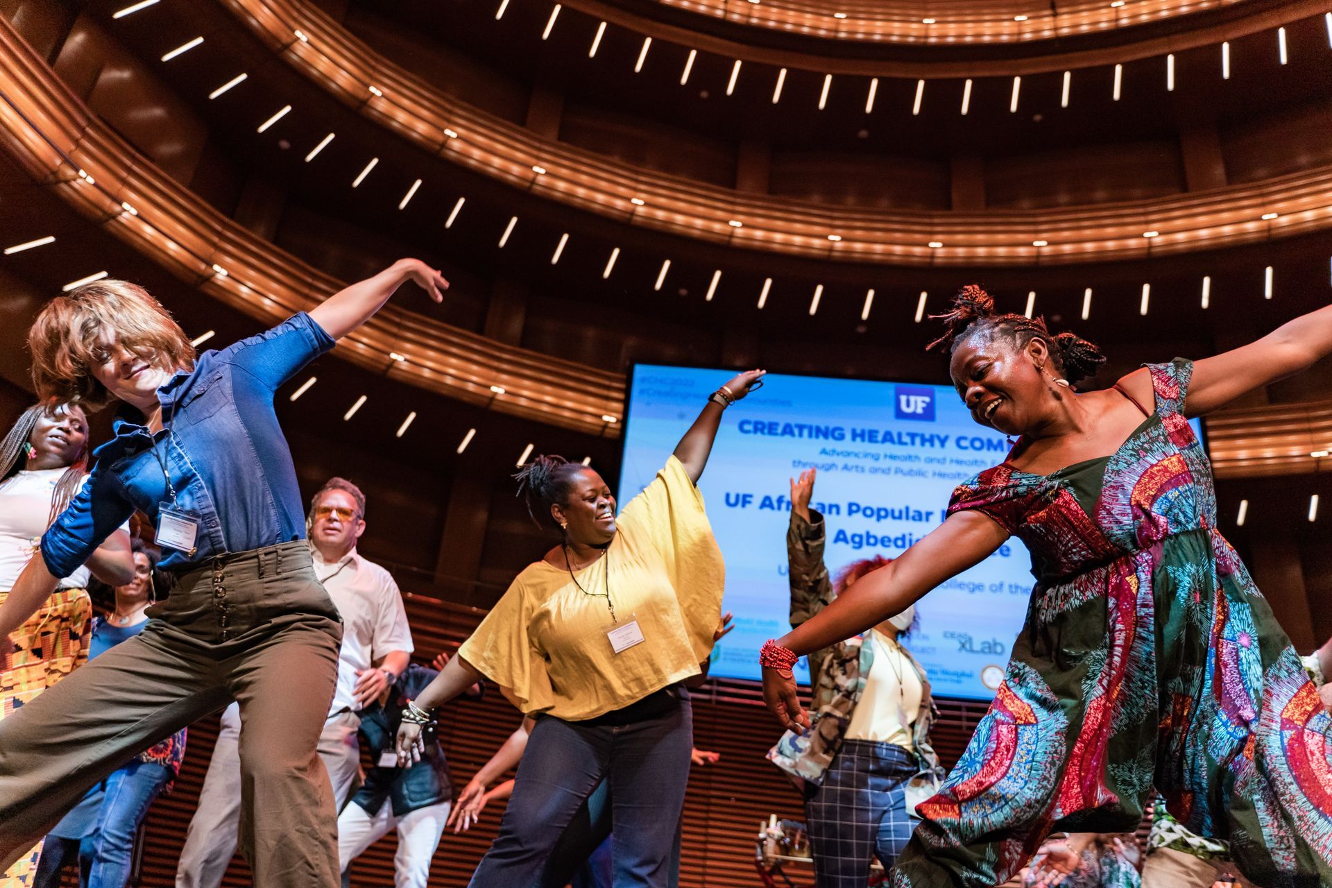 A group of people are dancing in a large auditorium.