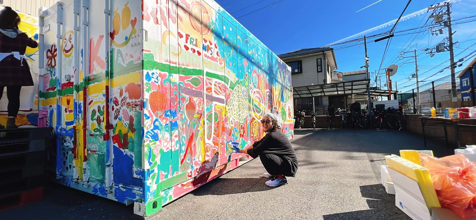 Artist Betty N. painting at the base of a shipping container that has been repurposed to a mural