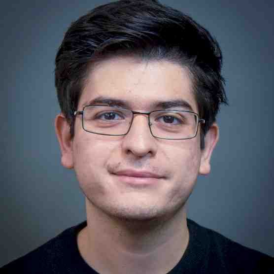 A young man wearing glasses and a black shirt is smiling for the camera.