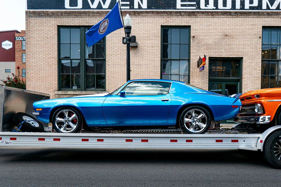 Blue classic sports car on a flatbed trailer outside an auto shop