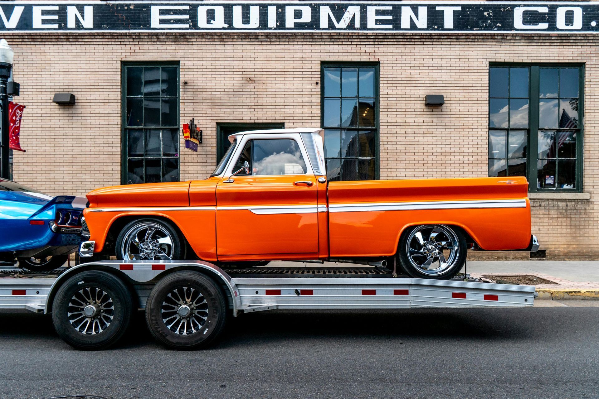 Orange classic pickup truck on a car hauler trailer outside a brick building
