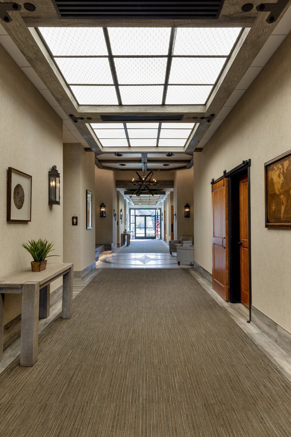 Funeral home hallway with traditional skylights, framed artwork, wall sconces, and carpeted walkway leading to entrance
