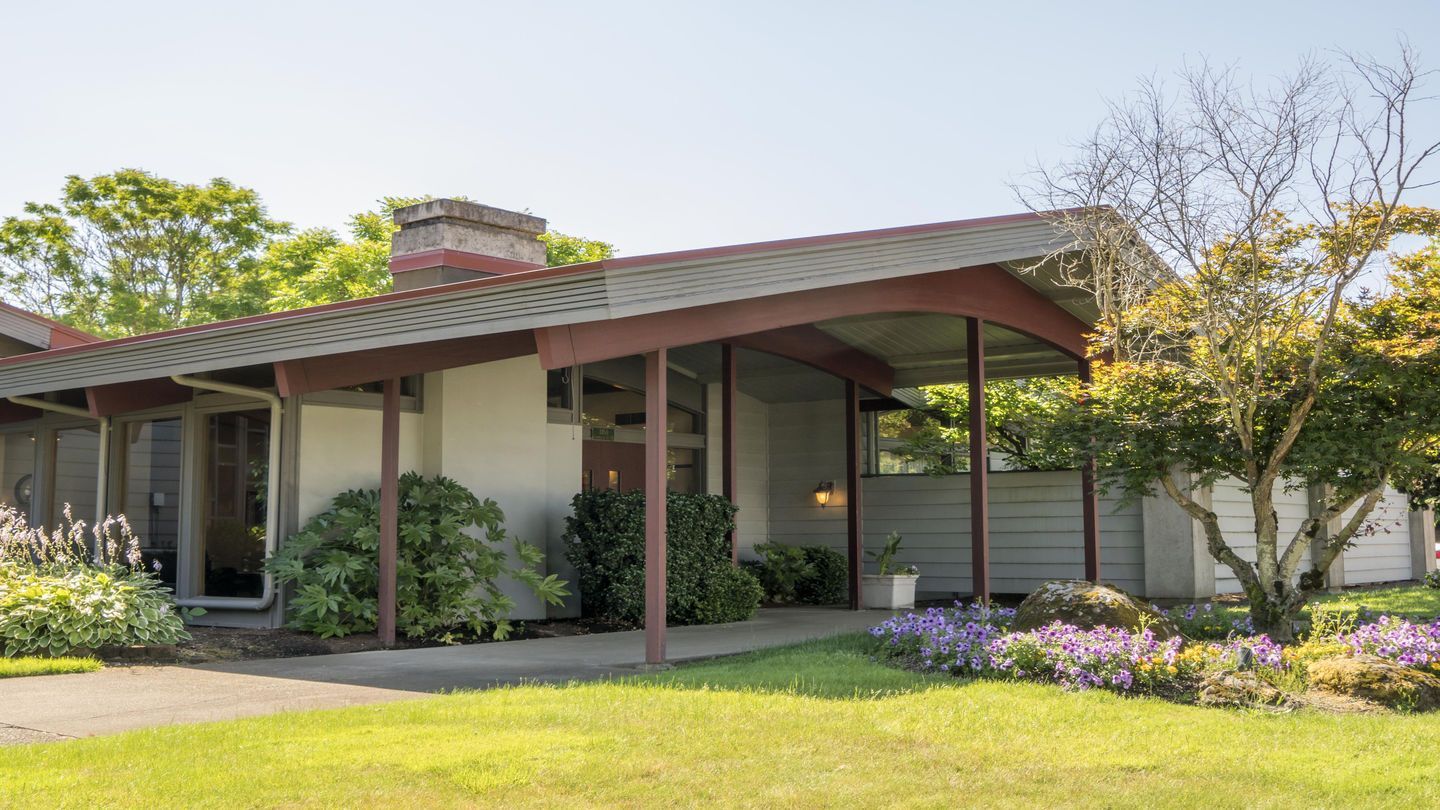 Mid-century modern funeral home building with covered entrance, mature trees, and flowering garden beds