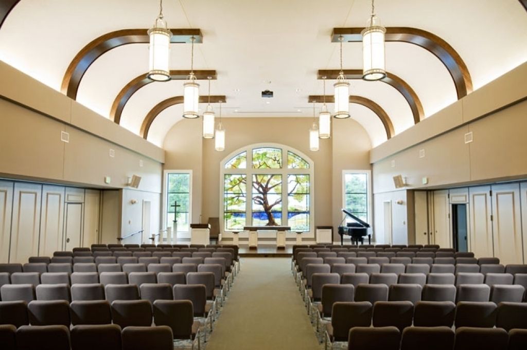 Chapel interior with rows of comfortable seating, arched ceiling, pendant lighting, and stained glass window
