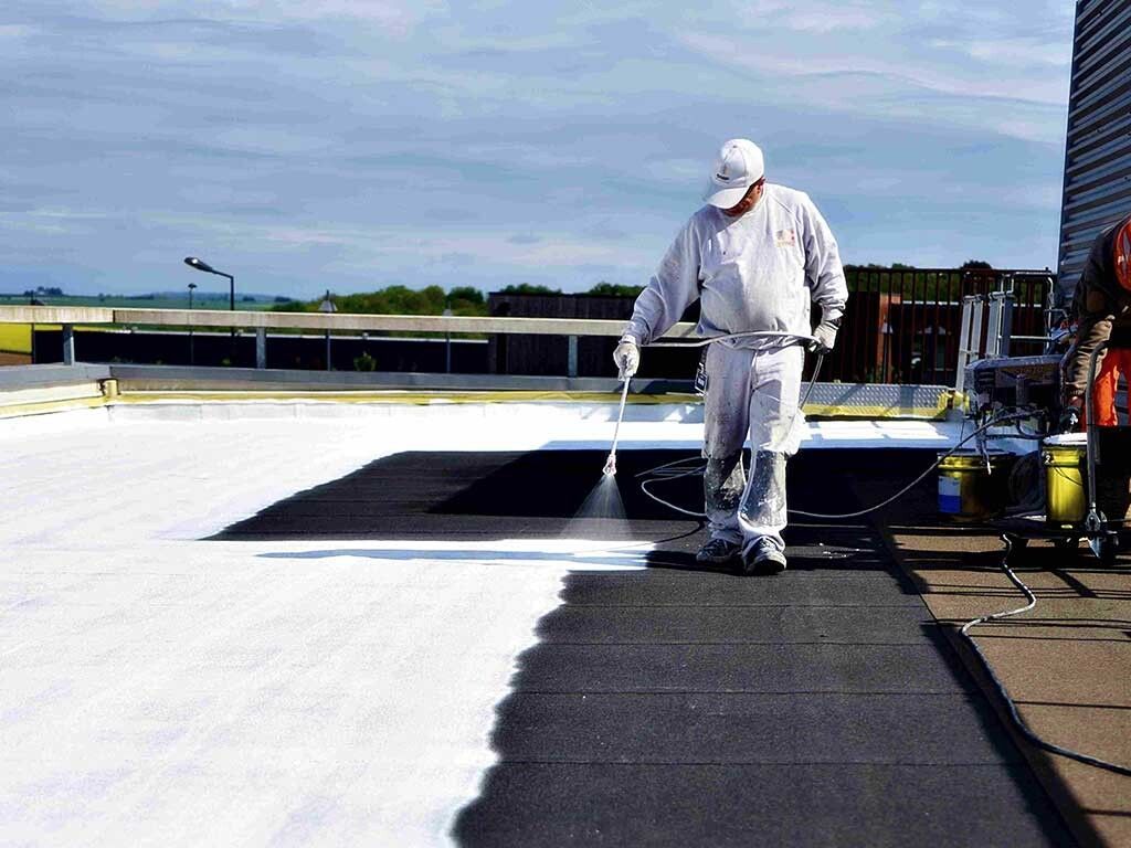 Commercial acrylic roof coating spray application showing contrast between coated and uncoated sections.