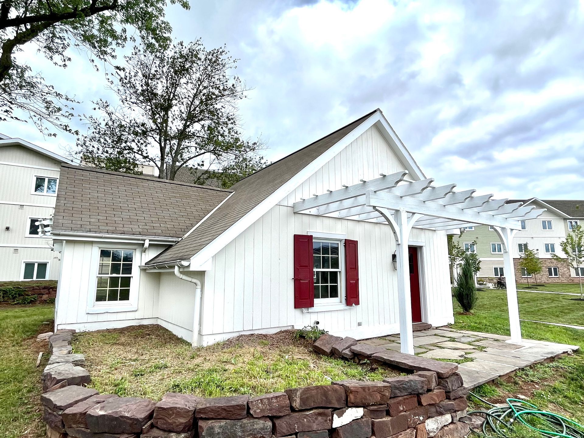 A small white house with red shutters and a pergola.