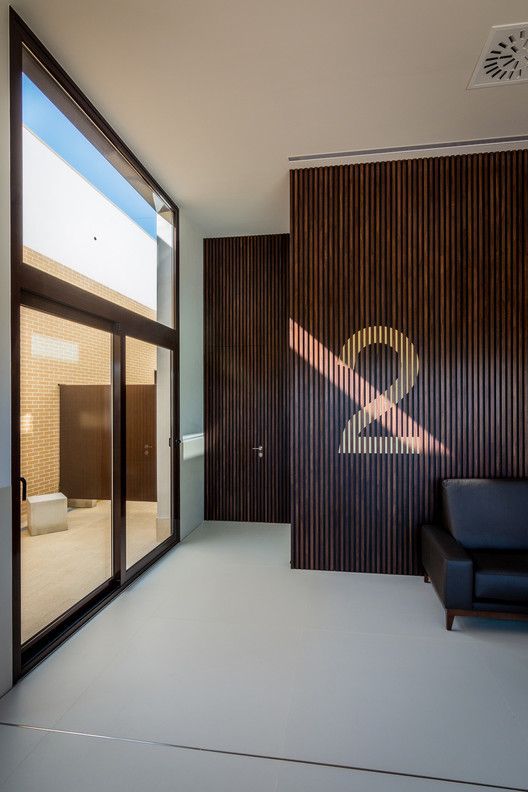 Contemporary funeral home entrance with wooden slat wall, glass doors, and minimalist seating area