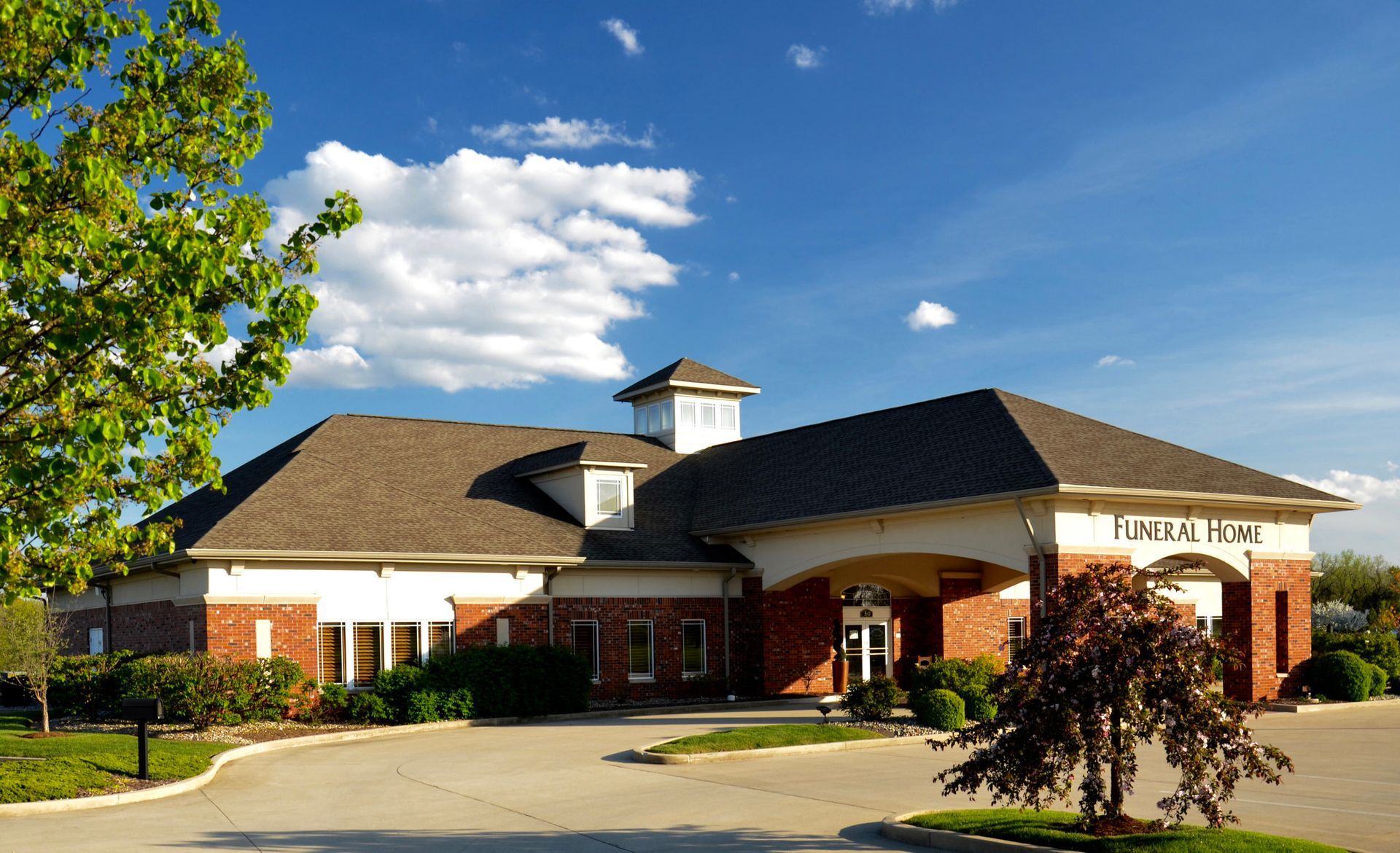 Modern funeral home exterior featuring brick and stucco construction, central cupola, and well-maintained landscaping