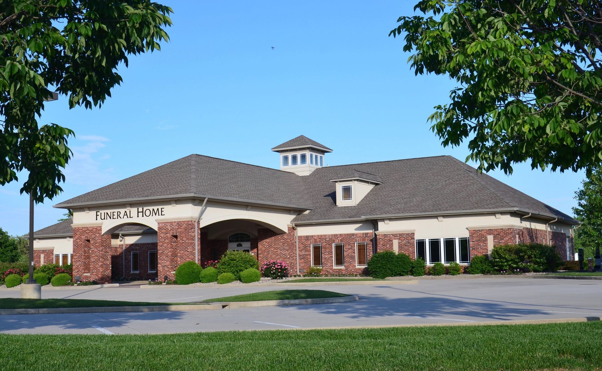 Contemporary funeral home exterior with brick facade, hip roof design, prominent signage, and landscaped grounds