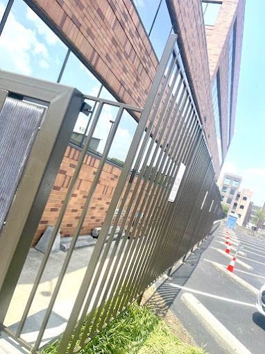 A metal fence is surrounding a parking lot in front of a brick building.