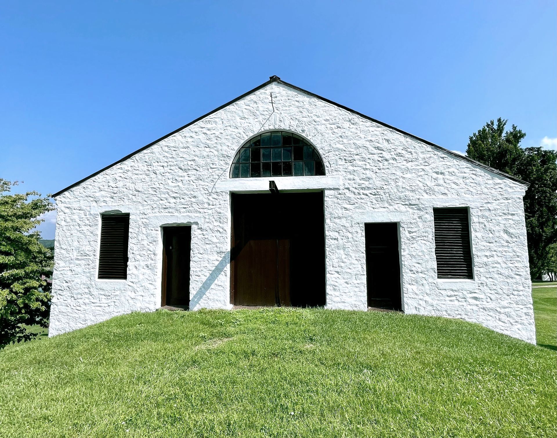 A white brick building is sitting on top of a grassy hill.