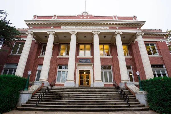 Classic university building entrance with red brick facade, white columns, steps leading to main doors, and surrounding trees