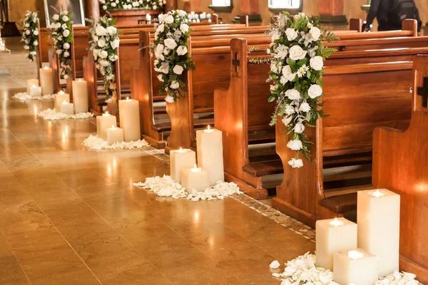 Church aisle decorated with white flowers, pillar candles, and rose petals for funeral service