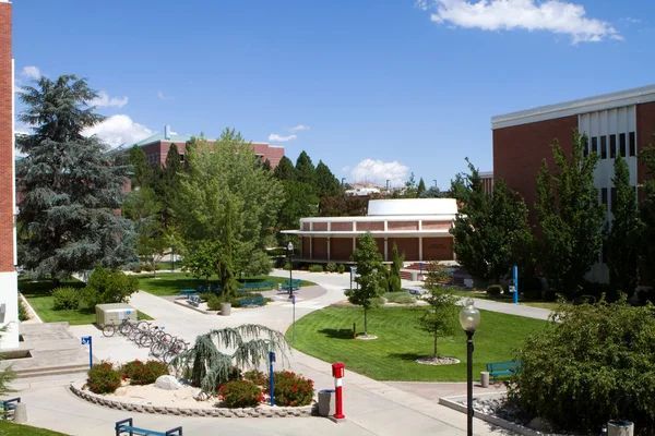 University campus courtyard view with red brick buildings, green lawns, trees, and student bike racks