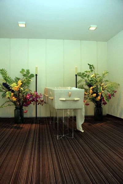 Simple memorial service room with white altar table, colorful flower arrangements, and striped wood flooring