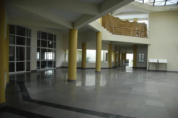 Grand school lobby with polished floors, yellow support columns, skylight above, and curved staircase to upper level