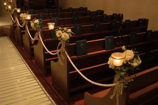Chapel pews adorned with white roses and rope detailing for memorial service ceremony
