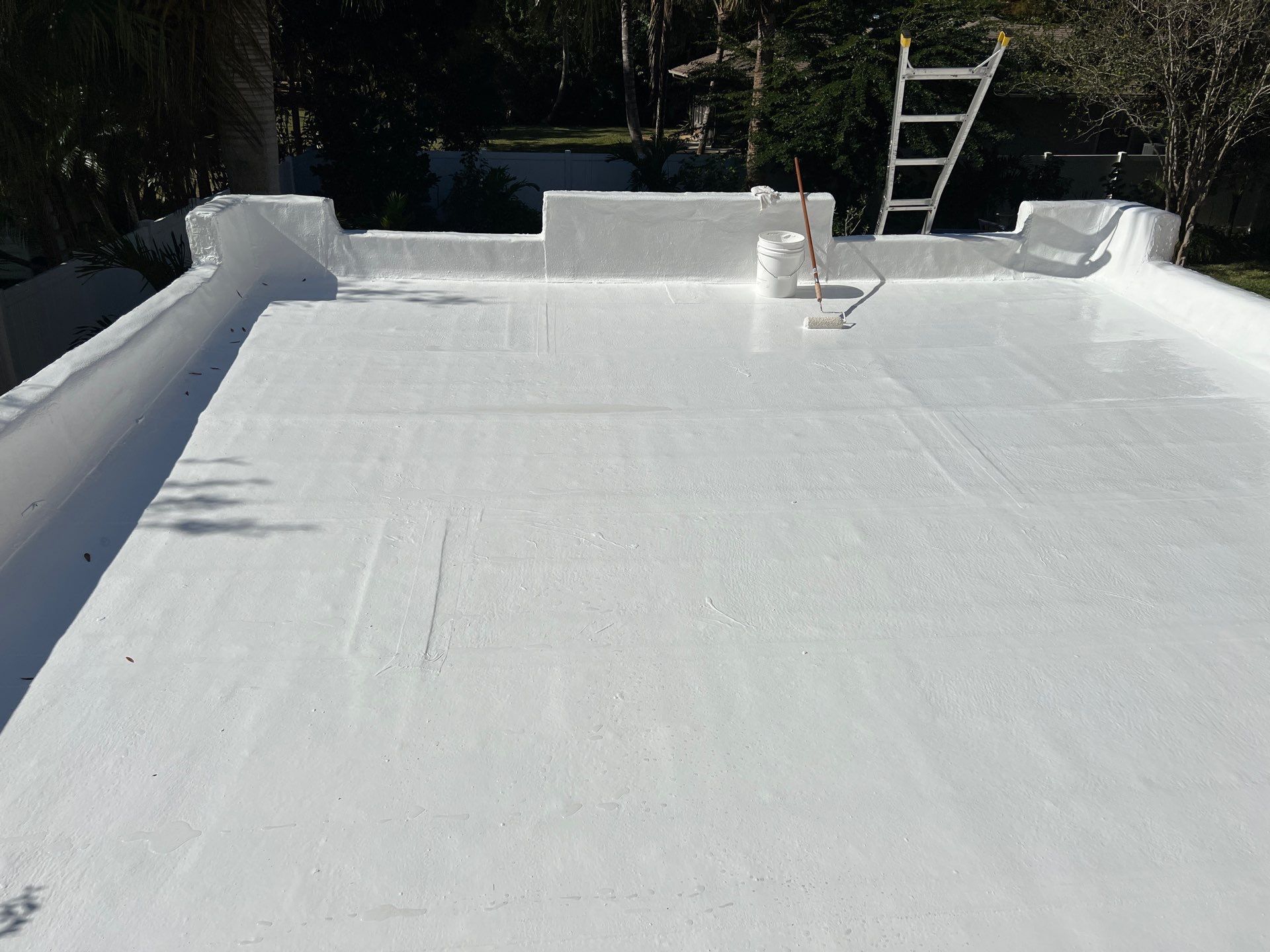 Completed white acrylic roof coating application on flat roof showing reflective surface finish.