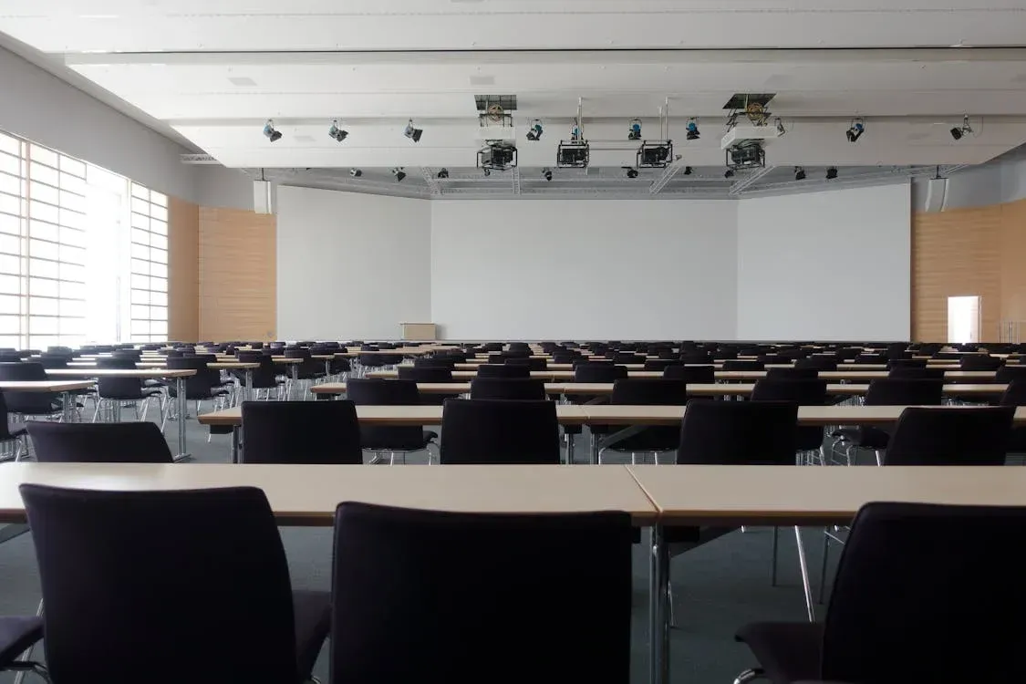 Modern lecture hall with black chairs, whiteboard projection screen, professional lighting equipment, and tiered seating