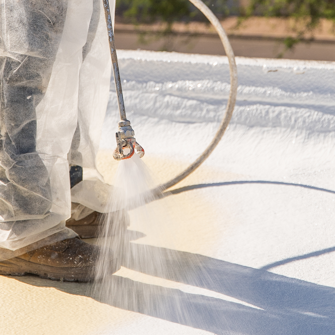 Professional spray application of acrylic roof coating using commercial equipment for waterproof protection.