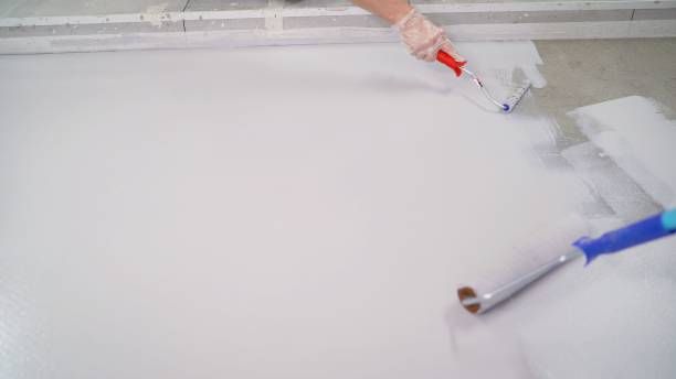 Professional applying acrylic roof coating with roller on commercial flat roof membrane surface.