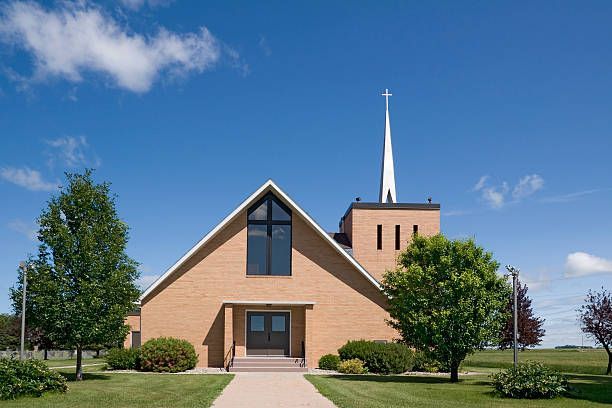 Modern brick church with tall steeple and large cross window against blue sky.