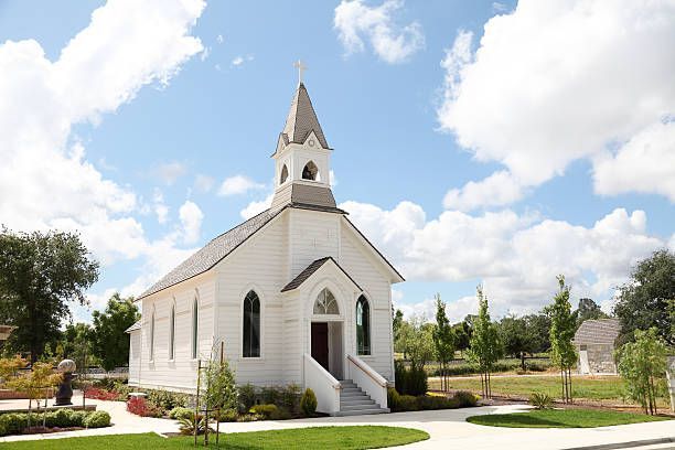 White country church with steeple surrounded by landscaped grounds.