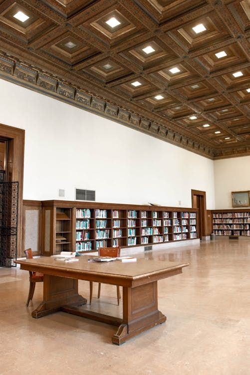 Historic library reading room with coffered ceiling, wooden bookshelves lining walls, and large wooden tables