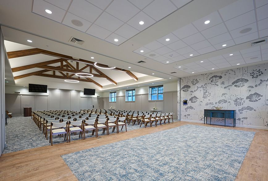 Modern funeral chapel with wooden beam ceiling, structured seating, decorative wallpaper, and carpeted floors