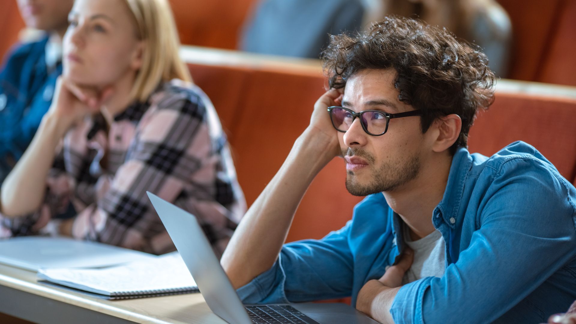 Students sitting at desks in a lecture hall with laptops, focusing attentively toward the front of the room.