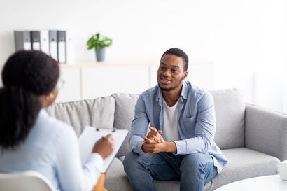 A therapist takes notes while listening to a patient sitting on a couch in an office setting. A therapist takes notes while listening to a patient sitting on a couch in an office setting.