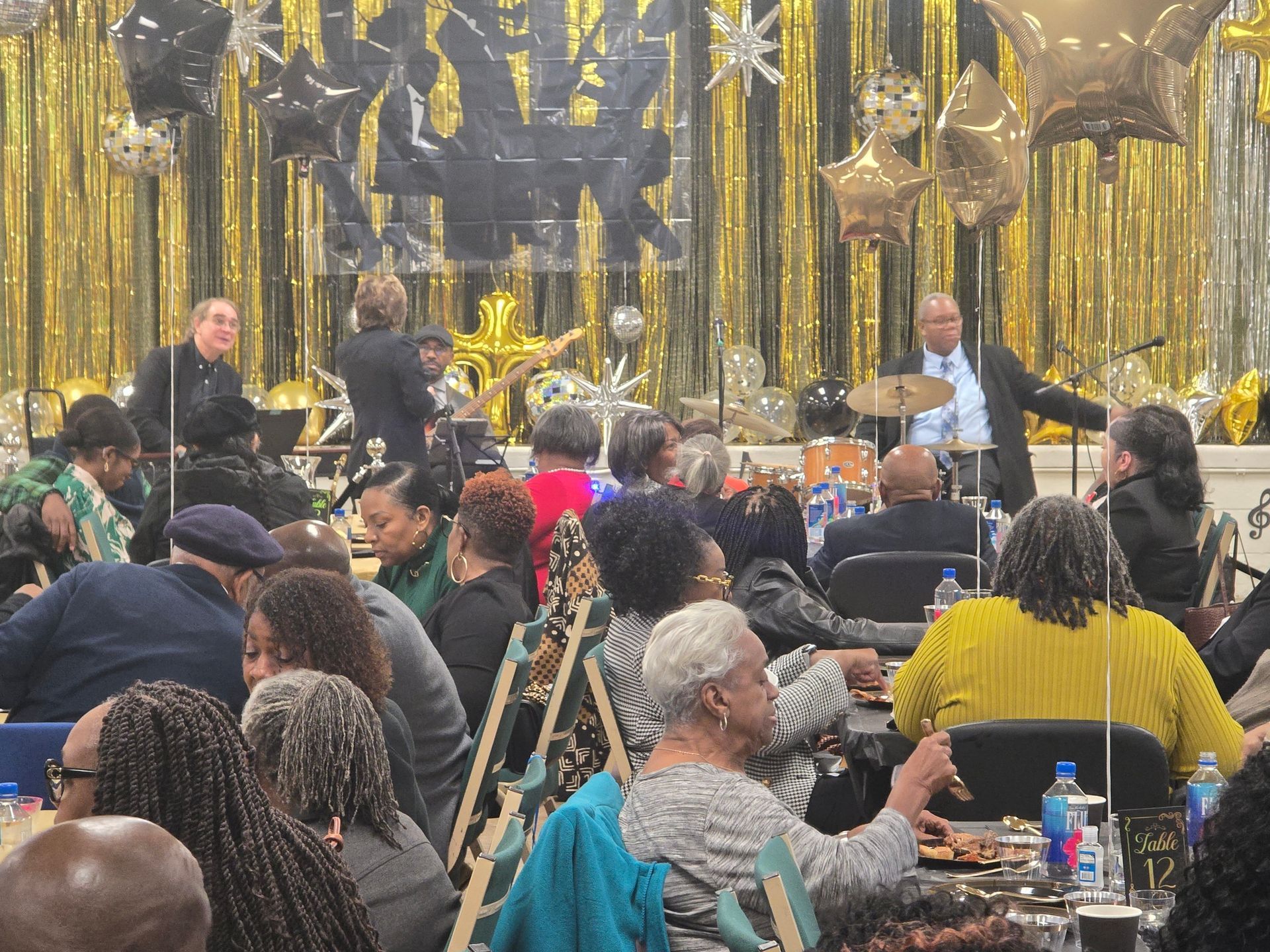 Audience at a formal event, band performing on stage with gold and silver decorations.