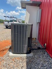 Outdoor HVAC unit next to a red building with a white truck in the background.