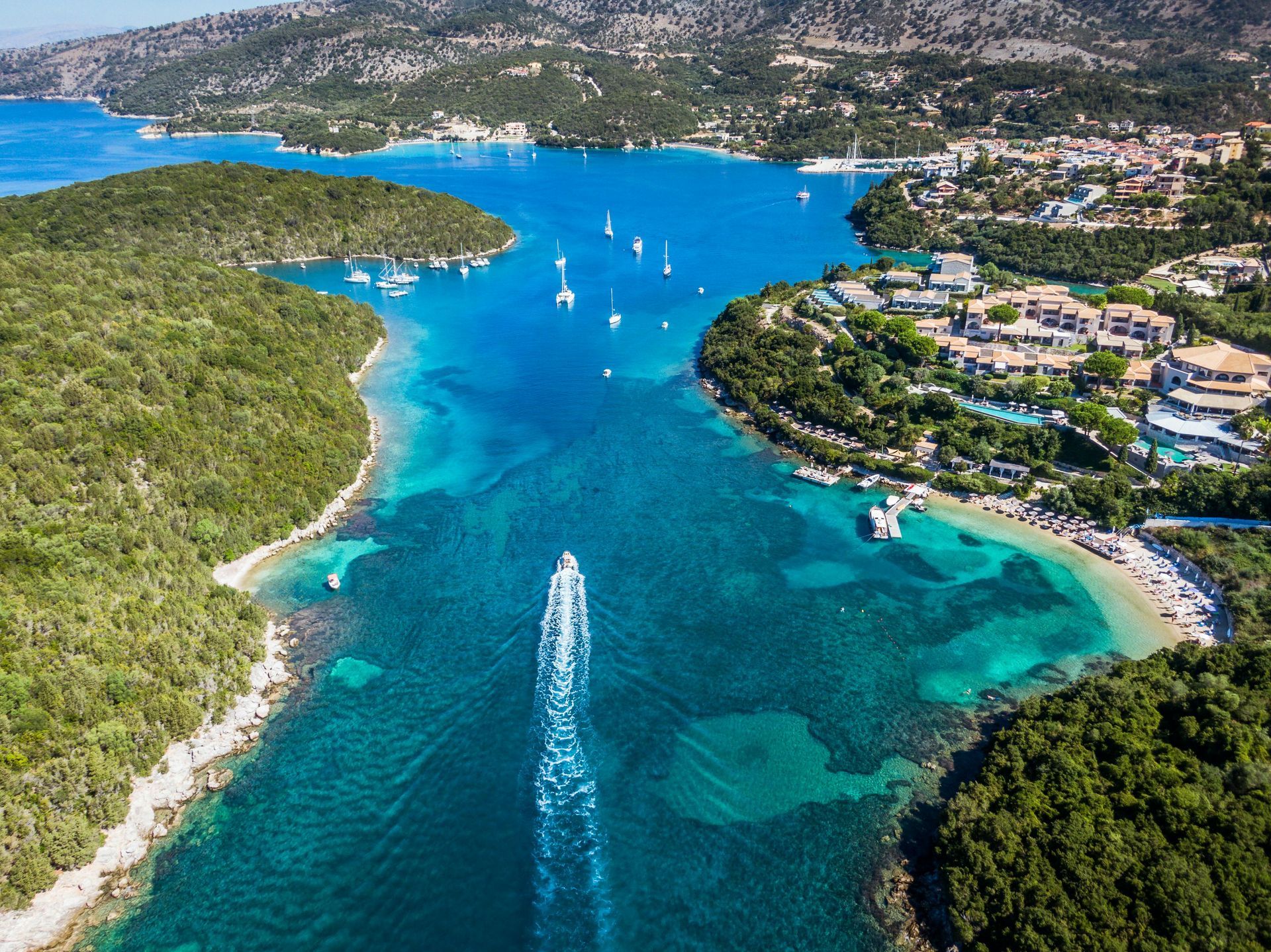 Aerial view of a turquoise bay with sailboats, a speedboat, and green islands along the coast