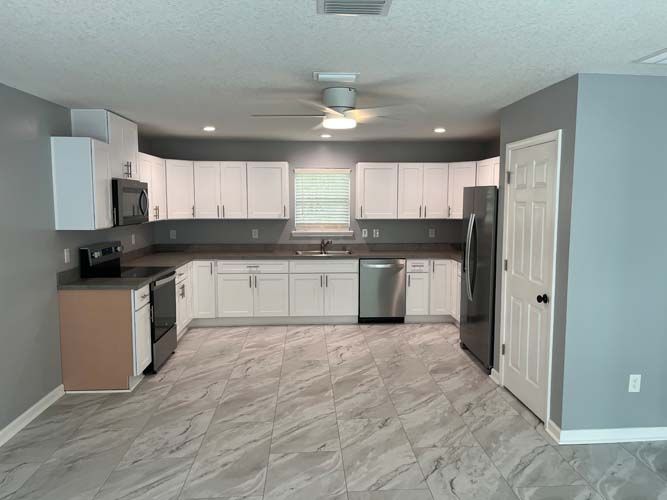 Bright modern kitchen with white cabinets, gray counters, stainless appliances, and light blue walls