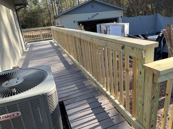 Wooden deck walkway with railing beside an HVAC unit, leading to a detached garage.