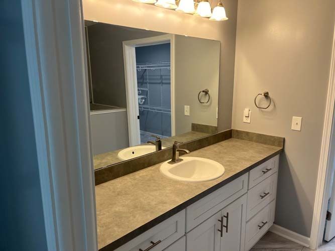 Bathroom vanity with sink, large mirror, and gray cabinets under warm lights