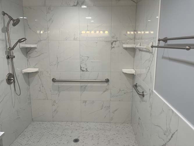 Accessible shower with grab bars, built-in shelves, and a fold-down seat in a white tiled bathroom