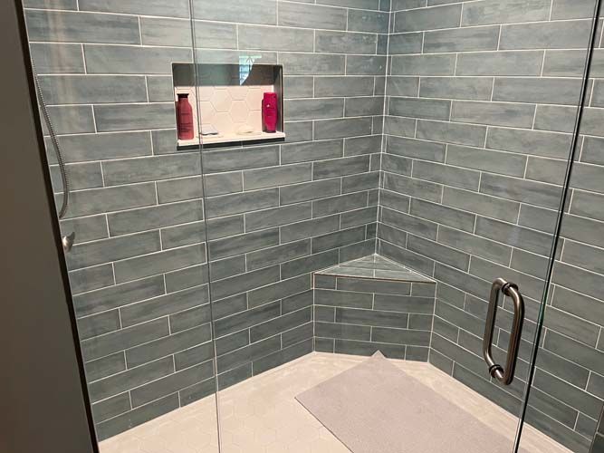 Gray-tiled shower stall with built-in shelf, niche, and metal grab bar.